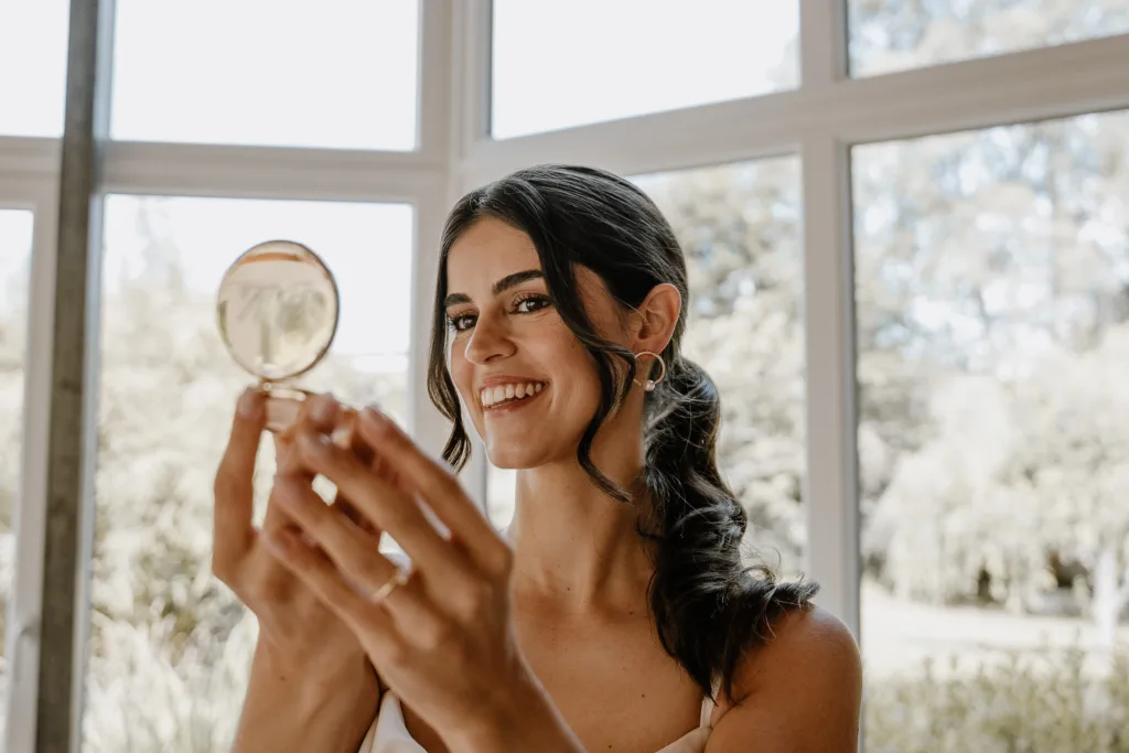 Braut betrachtet sich lächelnd mit Parfumflakon in der Hand