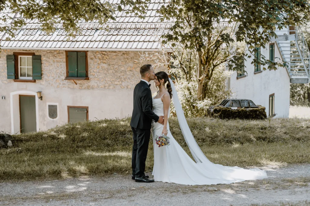 Brautpaar steht sich vor einem alten Gebäude gegenüber, der Bräutigam küsst die Braut auf die Stirn