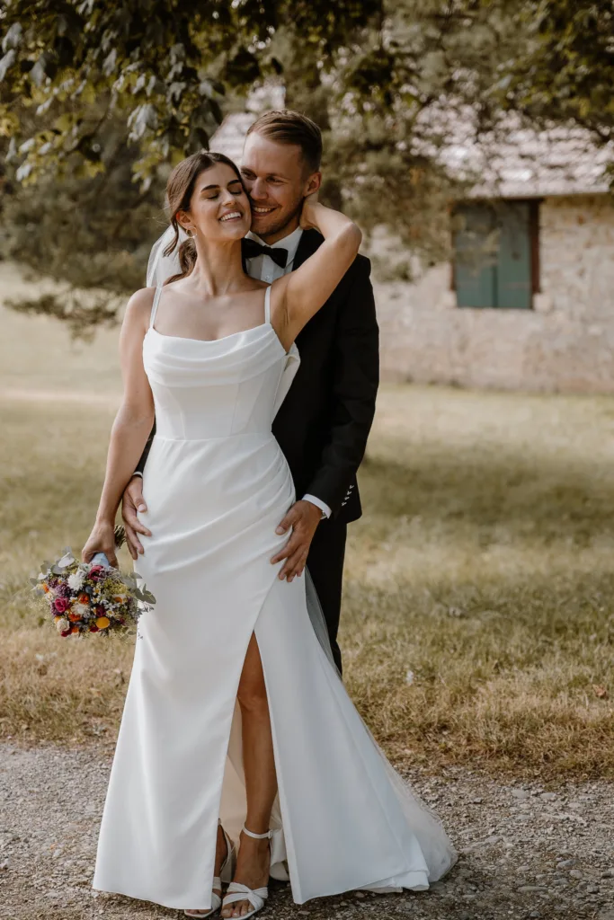 Bräutigam steht hinter der Braut und umarmt sie von hinten