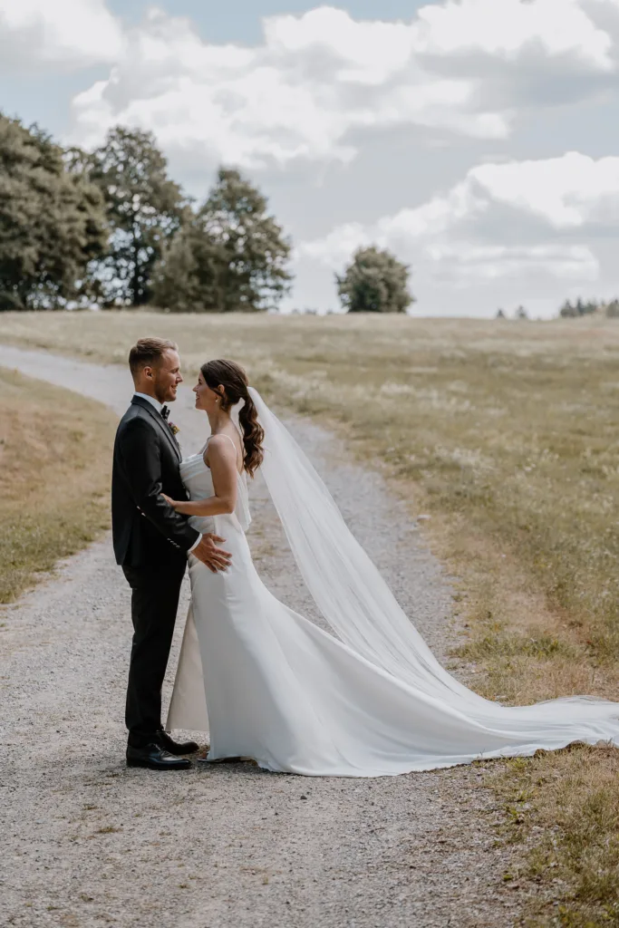 Brautpaar steht sich auf einem Feldweg gegenüber, der Schleier liegt im Wind