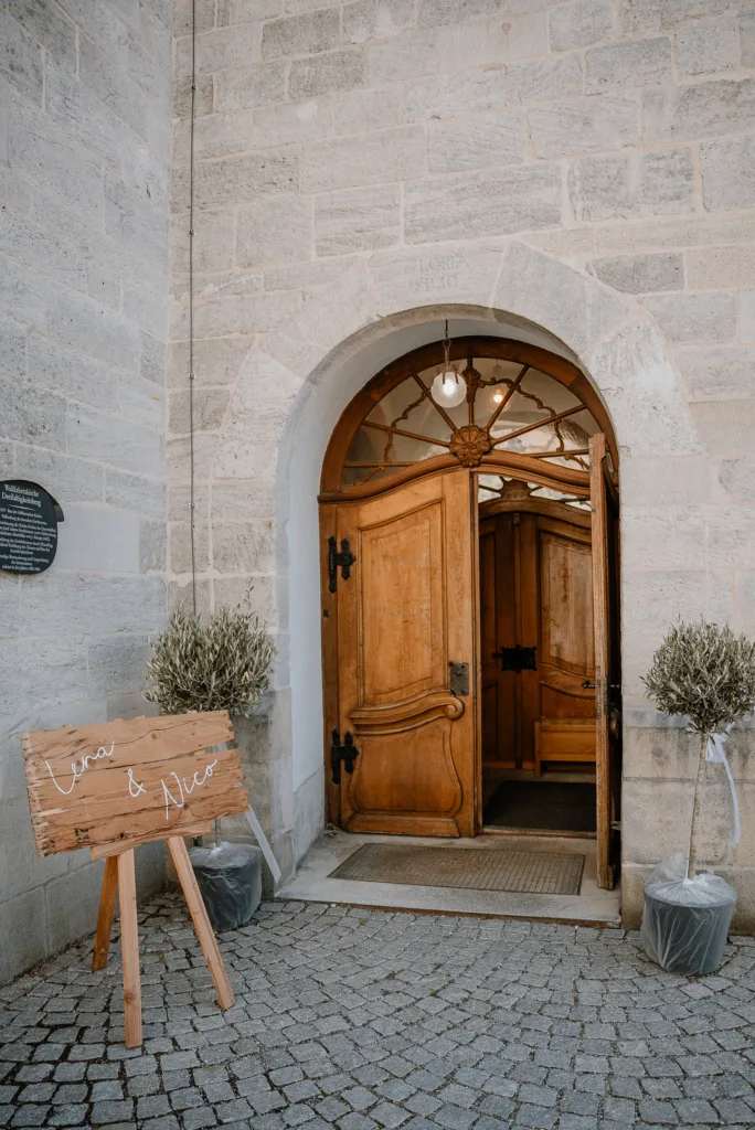 Offene Kirchentür mit Hochzeitsschild und Blumen