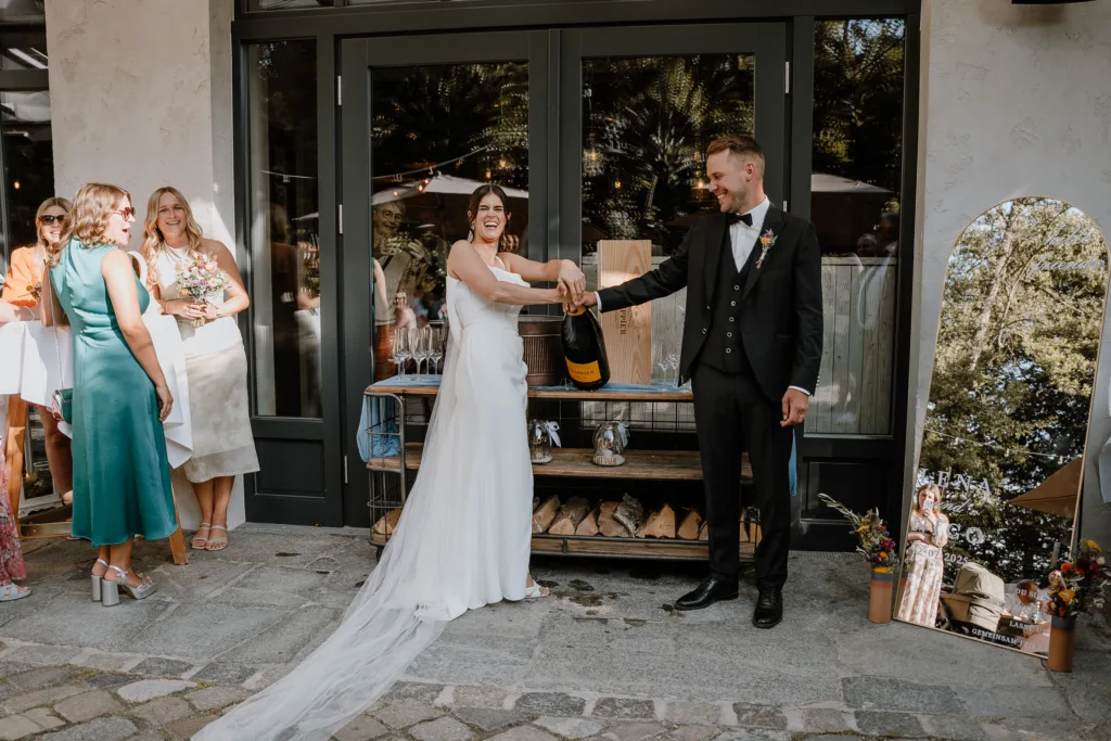 Braut öffnet Champagnerflasche gemeinsam mit dem Bräutigam