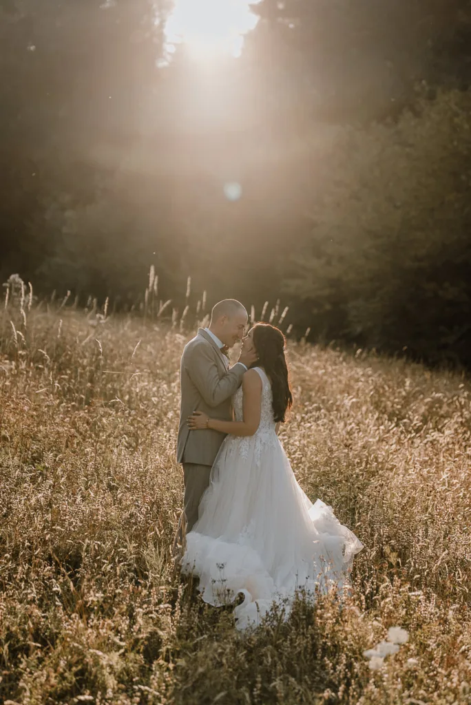 Brautpaar umarmt sich innig auf einer sonnendurchfluteten Wiese im goldenen Abendlicht. Romantisches Hochzeitsportrait bei einem natürlichen Paarshooting.